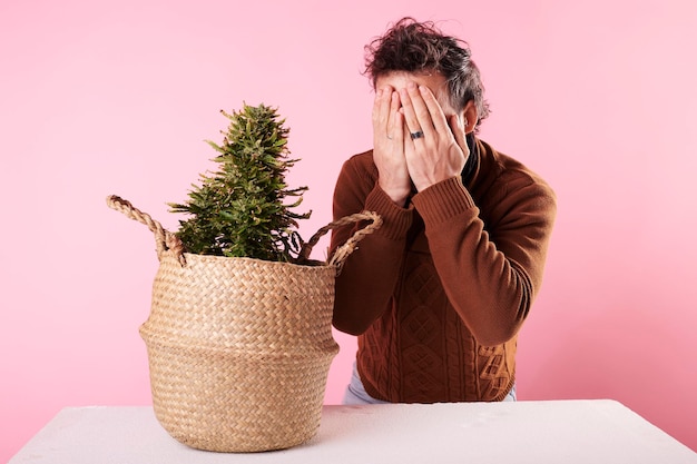 A young man surprised next to a marijuana plant with a pink background