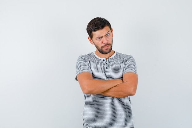 Young man in t-shirt keeping arms folded and looking pensive , front view.