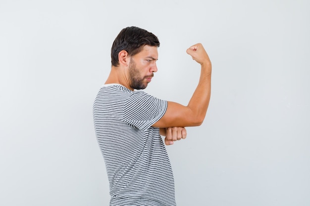 Young man in t-shirt showing muscles of arm and looking proud .