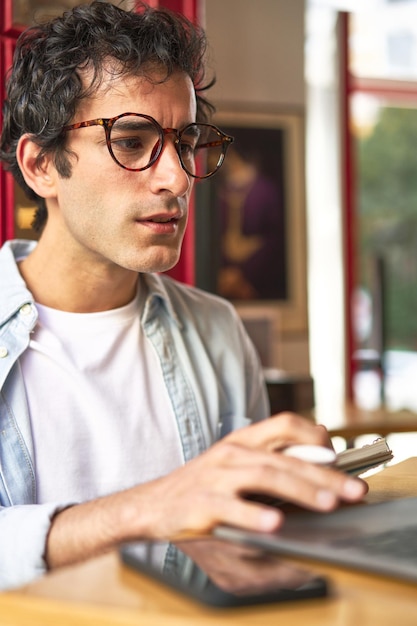 Young man takes notes while working on laptop at cozy cafe