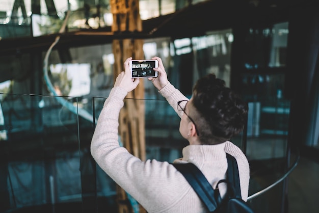 Young man taking photo while standing on floor with glass fence