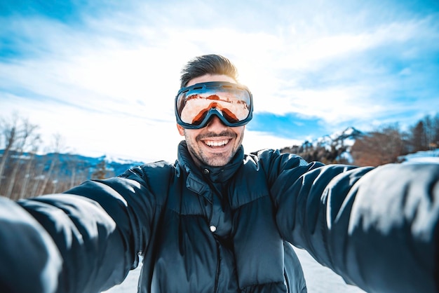 Young man taking selfie picture with smart cell phone hiking mountain on snowy slope