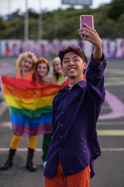 Young man taking a selfie with his friends behind holding the lgtbi flag Concept pride friendship freedom