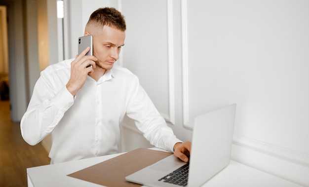 A young man talks on the phone and checks the information sitting at home in the kitchen