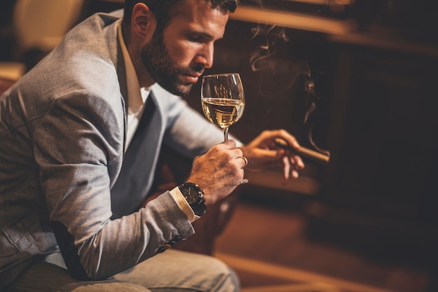 Young man tasting white wine and smoking cigar