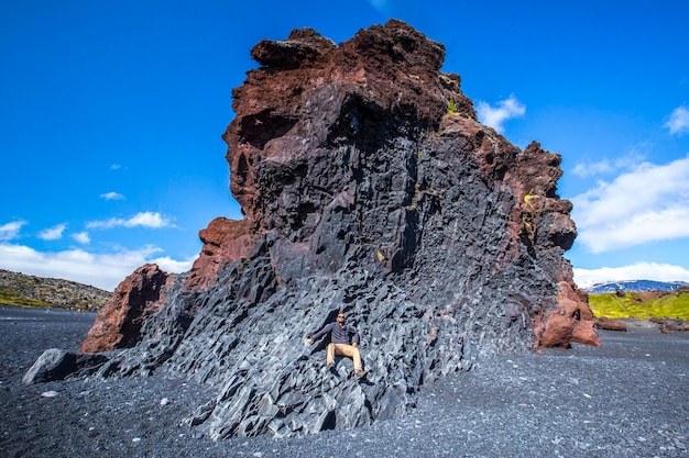 A young man on top of some rocks sitting on the black beach of the Snaefellsnes coast Iceland