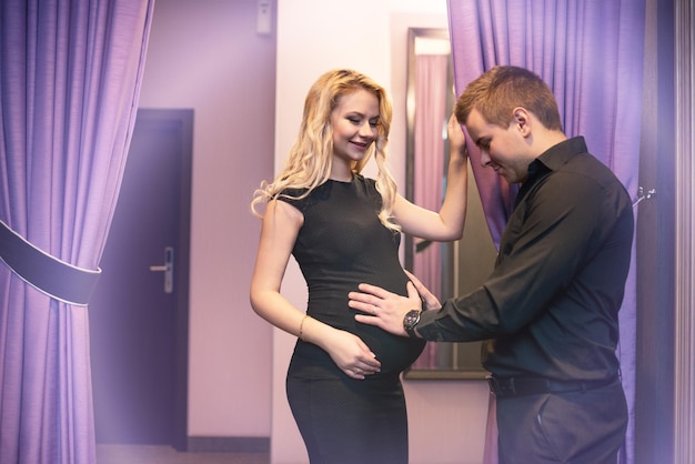 Young man touching belly of his beautiful pregnant wife and enjoy the replenishment in the family Concept of a young family and expectation of a child