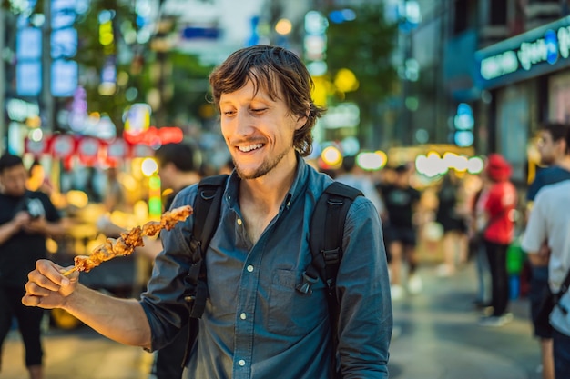 Young man tourist eating typical korean street food on a walking street of seoul spicy fast food