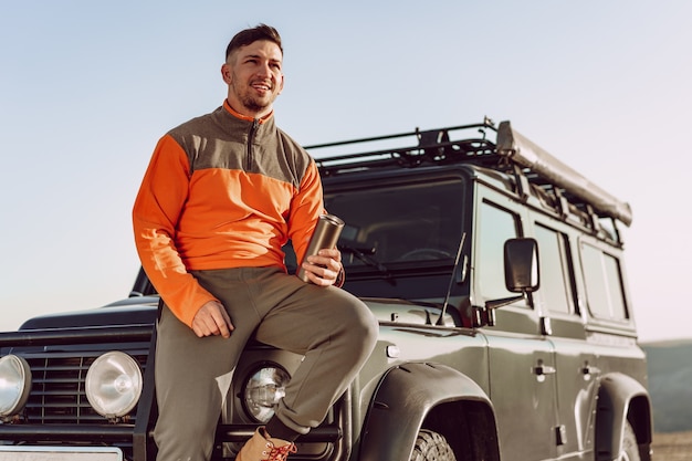 Young man traveler drinking from his thermocup while halt on a hike