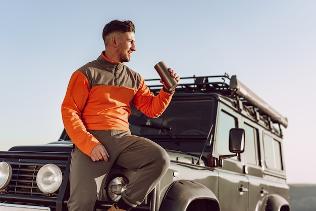 Young man traveler drinking from his thermocup while halt on a hike