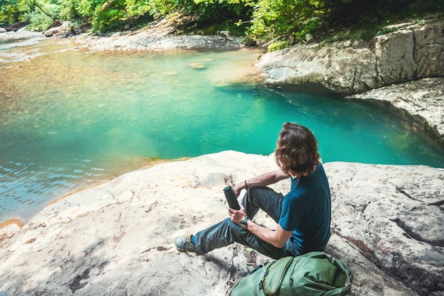 Young man traveler with backpack relaxing on the rocks of mountain lake Summer landscape