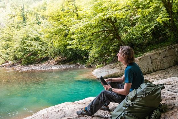 Young man traveler with backpack relaxing on the rocks of mountain lake