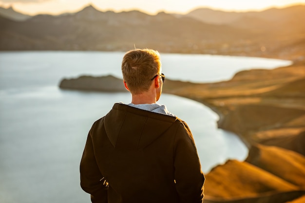 A young man travels along the mountain coast at sunset A man stands on a mountainside