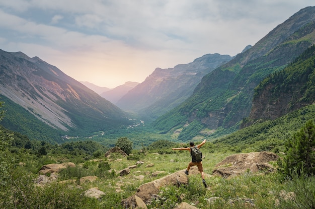 Young man trekking on the top of a green mountain during sunset