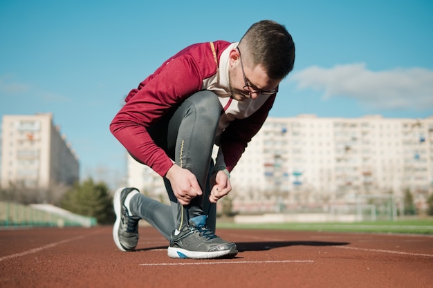 Young man tying shoelacesbefore jogging at stadium