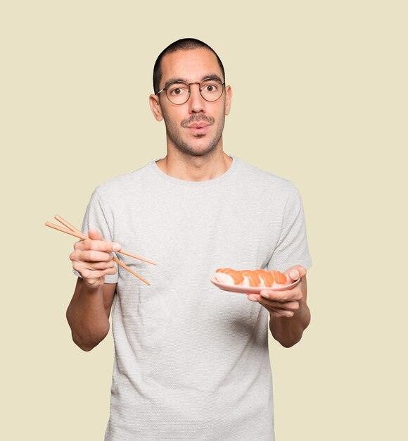 Young man using chopsticks to eat sushi