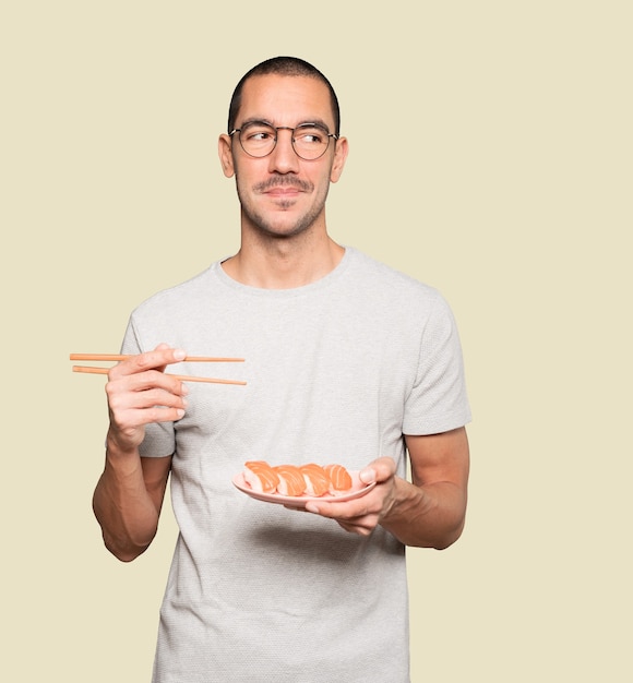 Young man using chopsticks to eat sushi