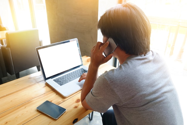 young man using laptop computer with blank copy space screen and calling mobile phone while sitting in cafe,flare sun