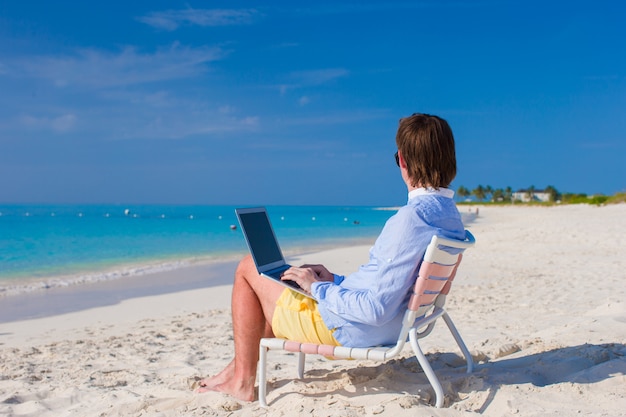 Young man using laptop on tropical beach