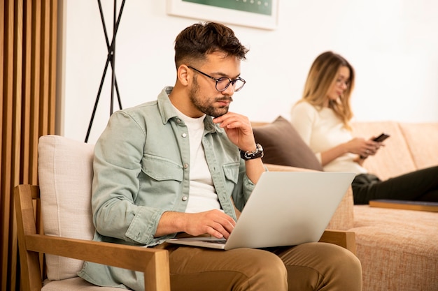 Young man using laptop while sitting with young woman at home