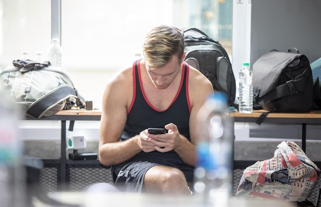 Photo young man using mobile phone while sitting in gym