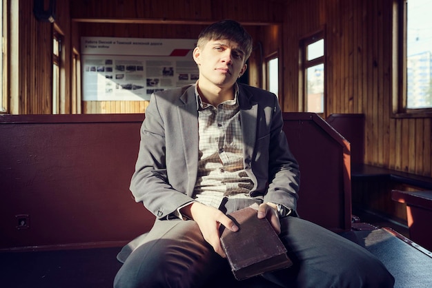 Young man in a vintage railway car is sitting reading a book and looking out the window