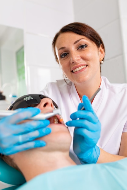 Young man visiting the dental office Dentist hands in protective gloves using ultrasound to clean patient's teeth Closeup of open mouth