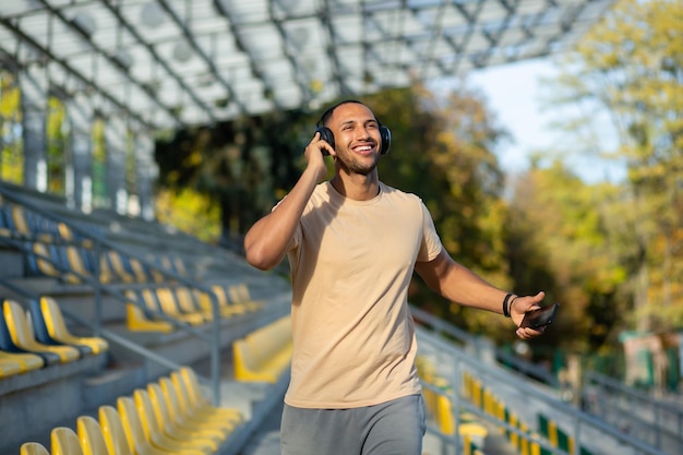 Young man walking in stadium after exercise and jogging in headphones listening to audiobook music