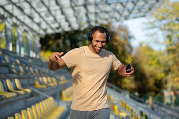 Young man walking in stadium after exercise and jogging in headphones listening to audiobook music