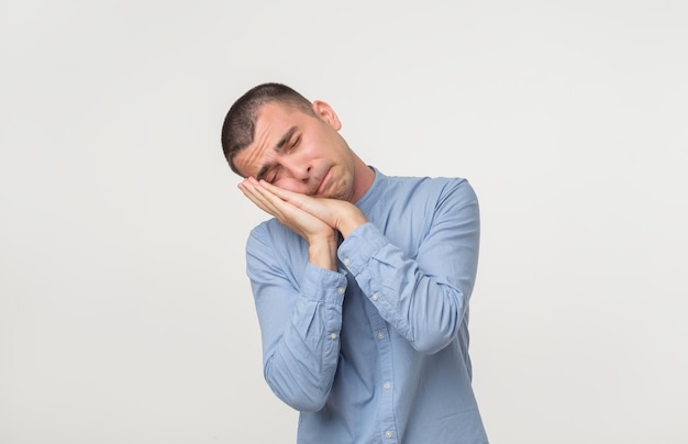 Young man wearing a blue outfit putting his palms like a pillow Looking sleepy and tired