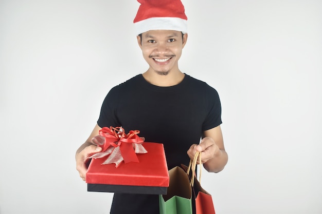 Young man wearing christmas hat holding red gift box and shopping bag