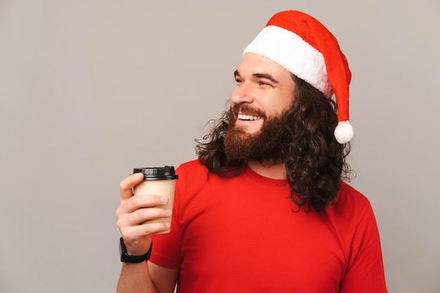 Young man wearing Christmas hat holds a take away cup of coffee and looks aside