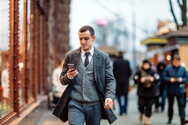 Young man wearing a coat walking down the street and using a cell phone