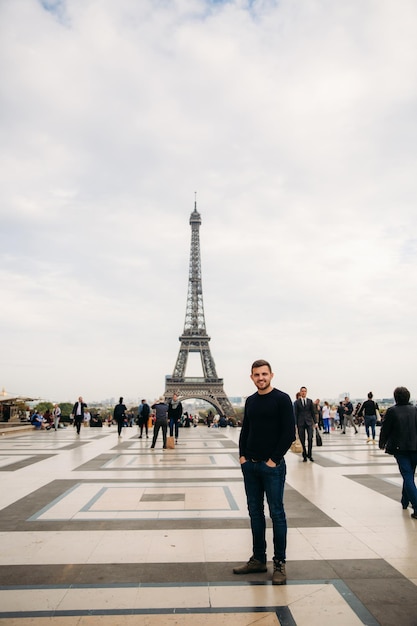 A young man wearing a dark blue jacket is standing on the background of the Eiffel Tower Sunny weather is autumn