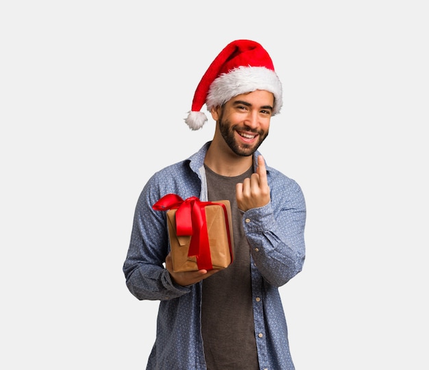 Young man wearing santa hat inviting to come