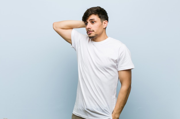 Young man wearing a white tshirt touching back of head, thinking and making a choice