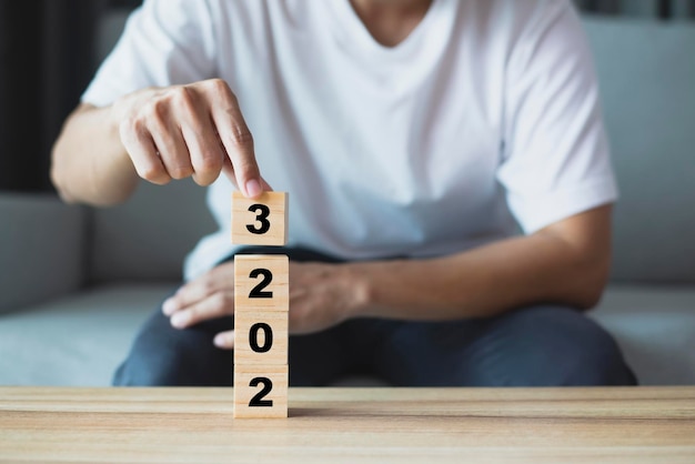 Young man wearing white tshirt using hand flipping wooden cubes blocks for change year 2022 to 2023 New year and holiday concept