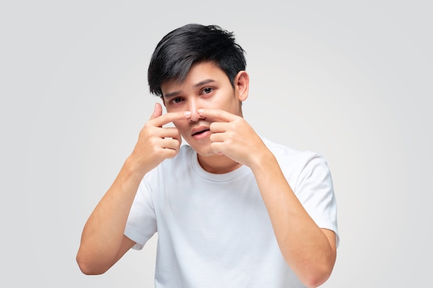 Young man wearing a white Tshirt using his hand squeezed a pimple on the tip of his nose.