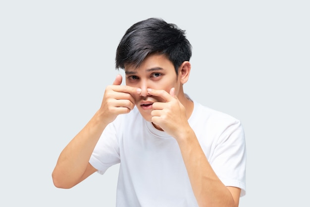 Young man wearing a white Tshirt using his hand squeezed a pimple on the tip of his nose.