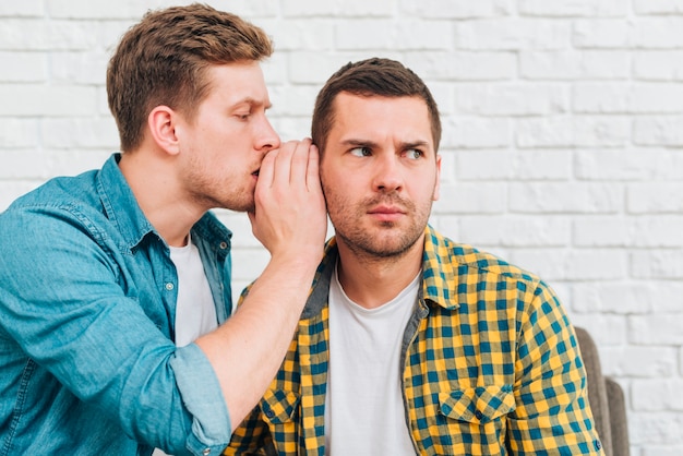 Young man whispering a secret in his friend's ear