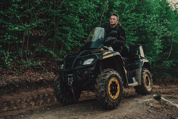 A young man in a white helmet rides through the woods on a Quad bike Extreme hobby A trip to ATV on the road from logs Quad Biking through the forest