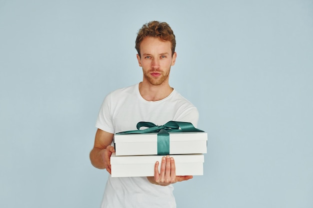 Young man in white shirt standing against wall and holds gift box