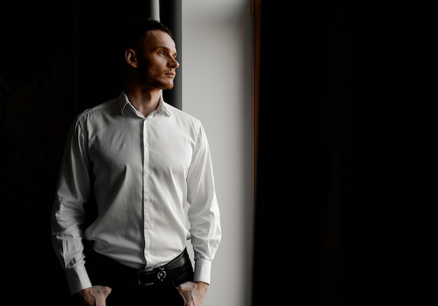 Young man in white shirt stares to the left side of the window. High quality photo