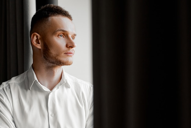 Young man in white shirt stares to the left side of the window. High quality photo