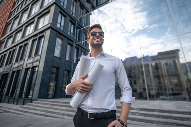 Young man in white shirt and sunglasses holding blueprints