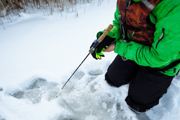 Young man on a winter fishing trip on a snowy lake fishes on a fishing rod