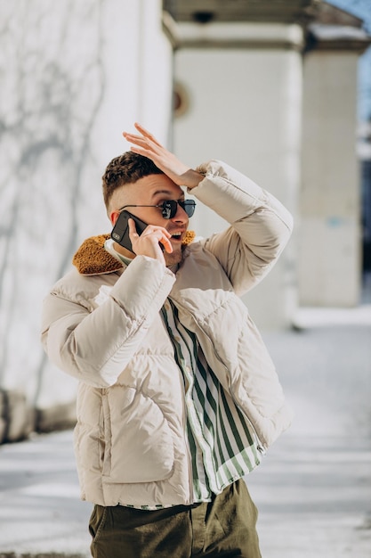 Young man in winter jacket using phone outside the street