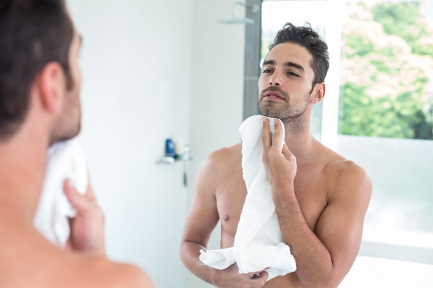 Young man wiping face while looking in mirror 