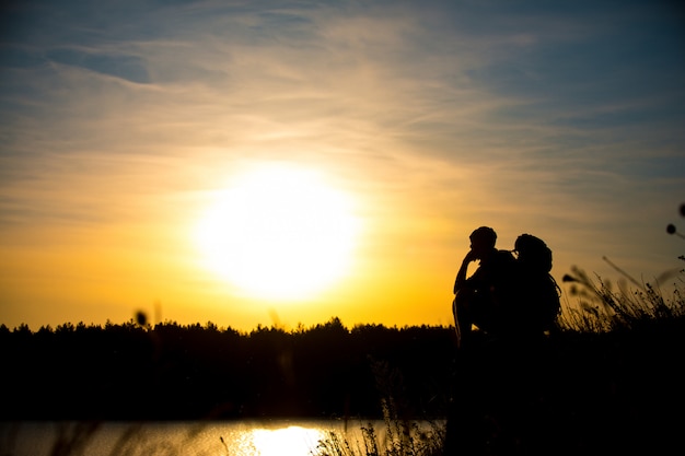 Young man with a backpack, enjoying the sunset on top of the mountain. Tourist traveler.