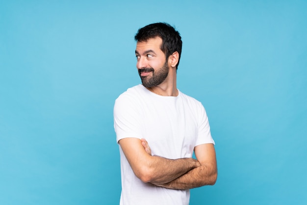 Young man with beard  over blue with arms crossed and happy